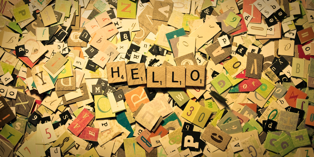 Image of cut out letters covering a surface, on top of them are Scrabble titles with letters spelling out the word "Hello"
