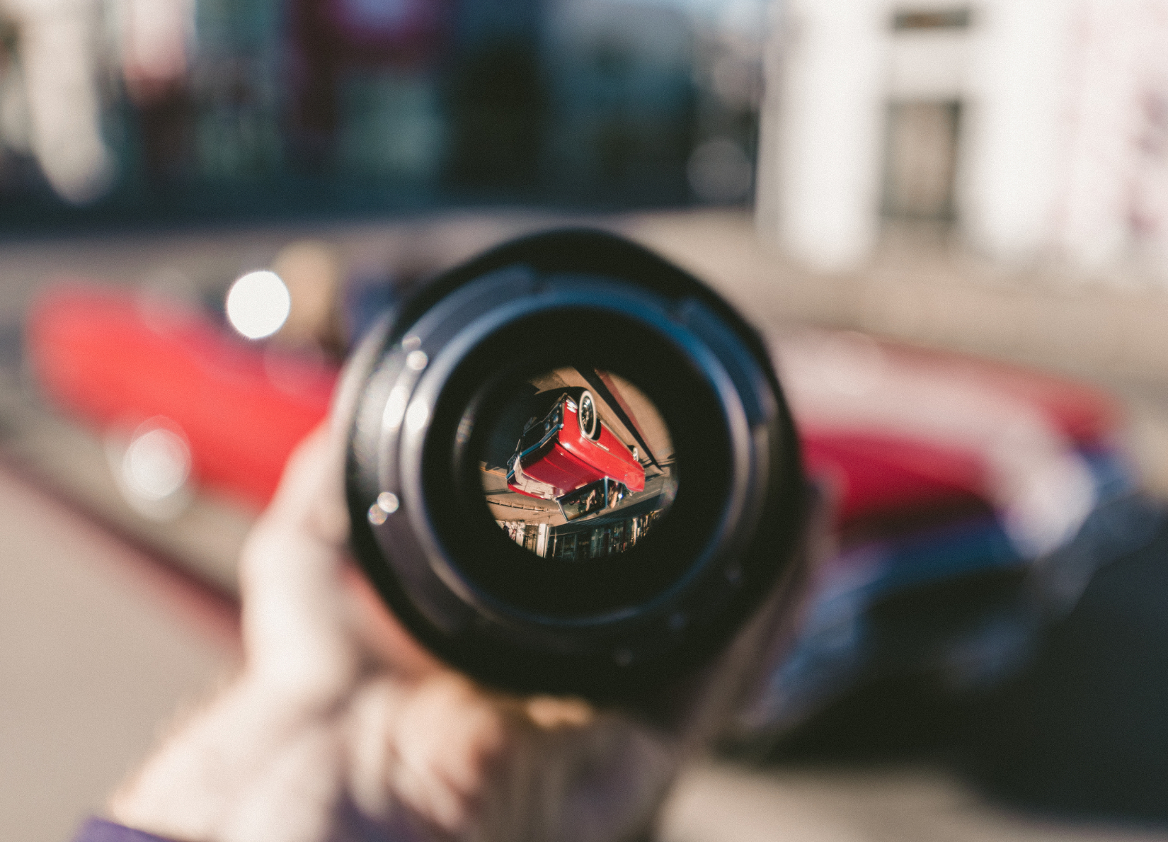 looking at a red car through a camera lens shown upside down and focused surrounded by a blurred view.